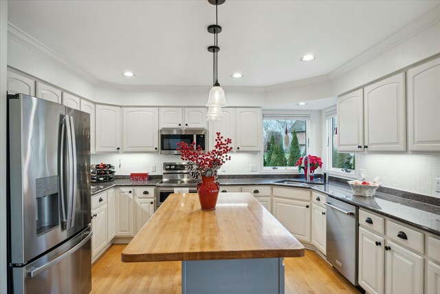 kitchen featuring a center island, wooden counters, white cabinets, hanging light fixtures, and appliances with stainless steel finishes