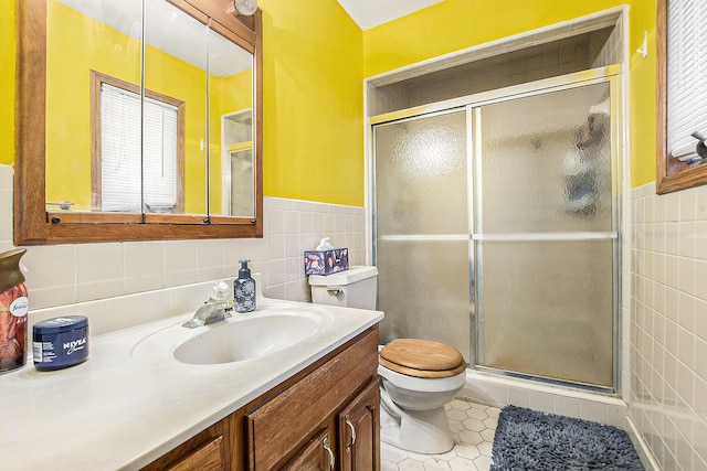 bathroom featuring tile patterned flooring, toilet, a shower with shower door, and tile walls