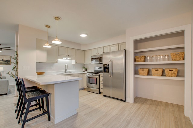 kitchen with a kitchen breakfast bar, stainless steel appliances, sink, pendant lighting, and light hardwood / wood-style floors