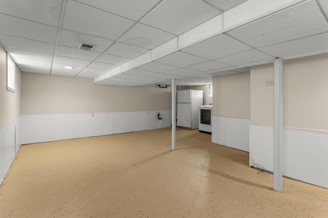 basement with a paneled ceiling and white fridge