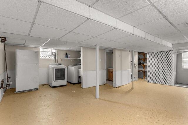 basement with a paneled ceiling, white fridge, and independent washer and dryer