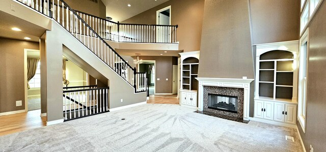 unfurnished living room with built in features, a chandelier, a multi sided fireplace, a high ceiling, and light hardwood / wood-style floors