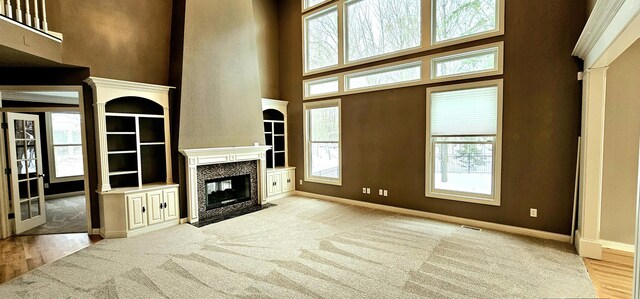 unfurnished living room with a high end fireplace, light hardwood / wood-style floors, a towering ceiling, and a wealth of natural light