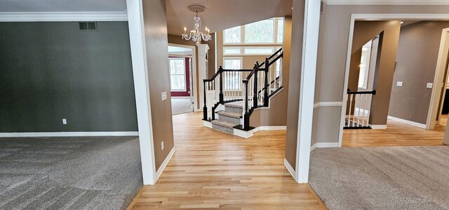 entrance foyer with a notable chandelier, light hardwood / wood-style floors, ornamental molding, and vaulted ceiling