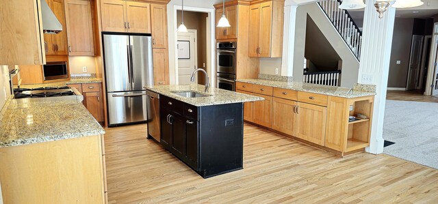 kitchen with sink, hanging light fixtures, stainless steel appliances, a center island with sink, and light wood-type flooring