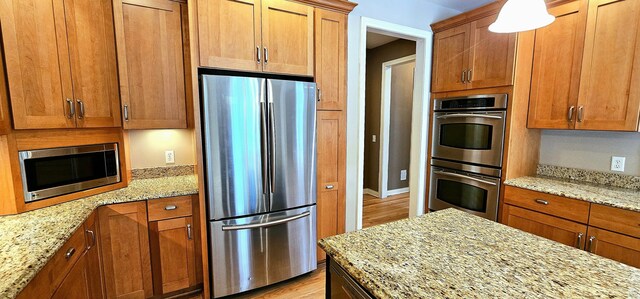 kitchen featuring stainless steel appliances, light stone counters, and light hardwood / wood-style flooring