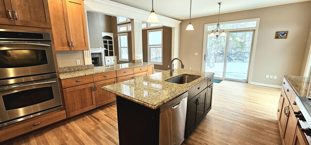 kitchen featuring pendant lighting, a center island with sink, sink, light wood-type flooring, and appliances with stainless steel finishes