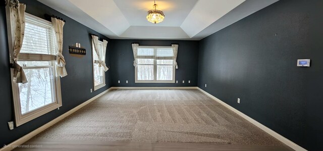 spare room with carpet flooring, a wealth of natural light, a tray ceiling, and a chandelier