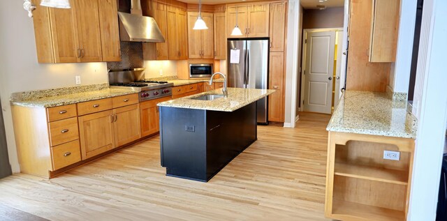 kitchen featuring light stone countertops, wall chimney exhaust hood, sink, pendant lighting, and light hardwood / wood-style flooring