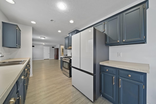 kitchen featuring sink, refrigerator, stainless steel range with gas cooktop, and blue cabinets