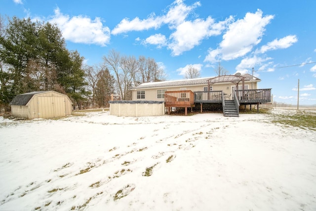 snow covered back of property featuring a wooden deck and a storage shed