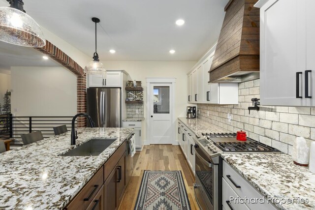 kitchen with light wood-type flooring, custom exhaust hood, stainless steel appliances, sink, and white cabinets