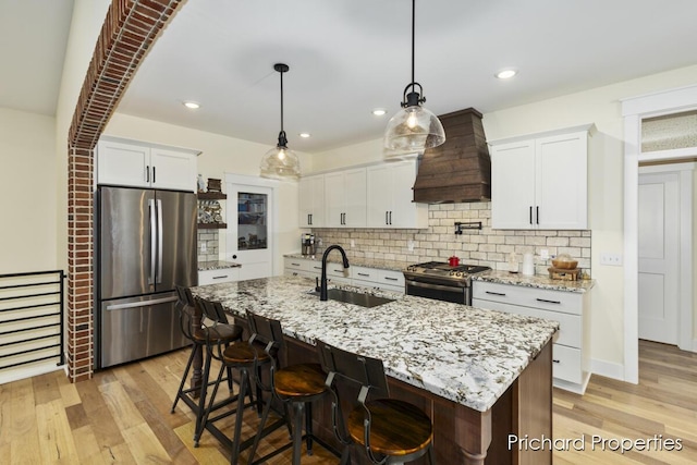 kitchen featuring custom exhaust hood, stainless steel appliances, sink, light hardwood / wood-style floors, and white cabinetry