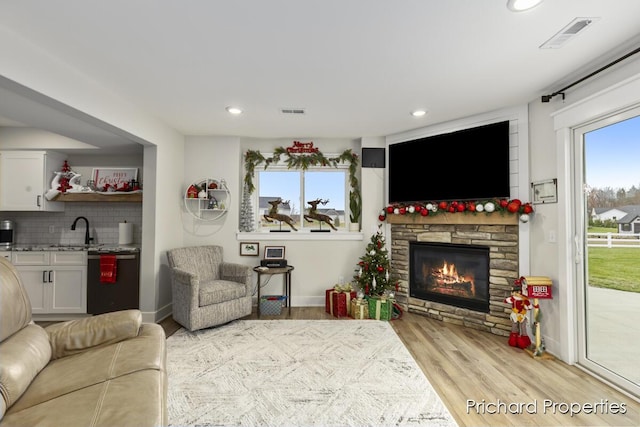 living room featuring light hardwood / wood-style floors, a stone fireplace, and sink