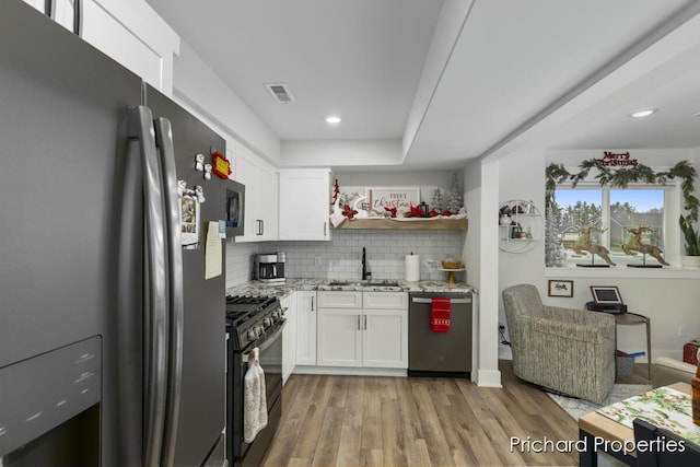 kitchen featuring light wood-type flooring, light stone counters, stainless steel appliances, sink, and white cabinetry