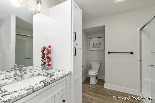 bathroom with hardwood / wood-style floors, vanity, a shower with door, and toilet