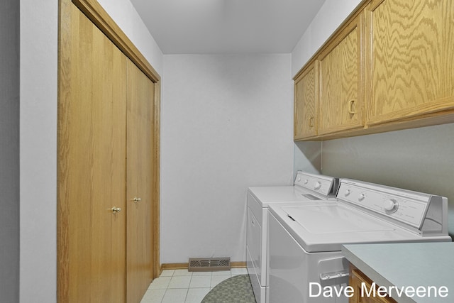 laundry room with washing machine and clothes dryer, light tile patterned floors, and cabinets