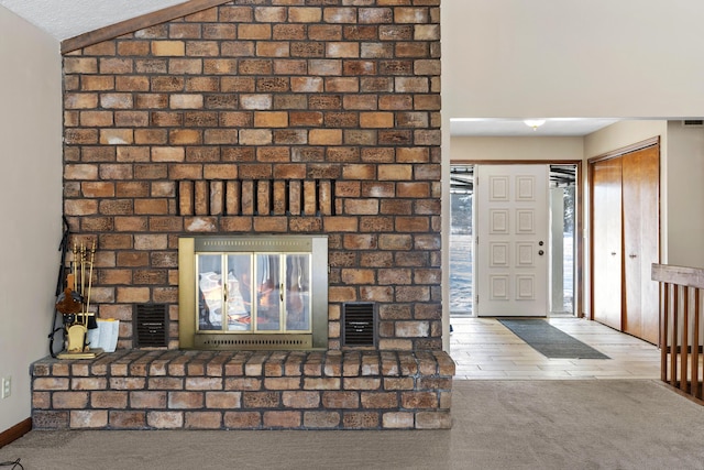 carpeted entrance foyer with a fireplace, vaulted ceiling, and a textured ceiling