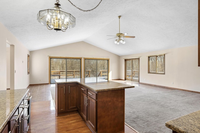 kitchen featuring pendant lighting, lofted ceiling, light stone countertops, and a textured ceiling