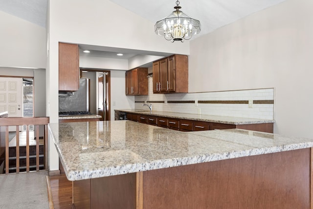 kitchen featuring light stone countertops, sink, kitchen peninsula, and decorative light fixtures