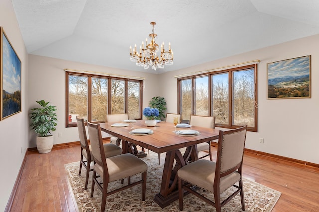 dining room featuring vaulted ceiling, a chandelier, light hardwood / wood-style floors, and a textured ceiling