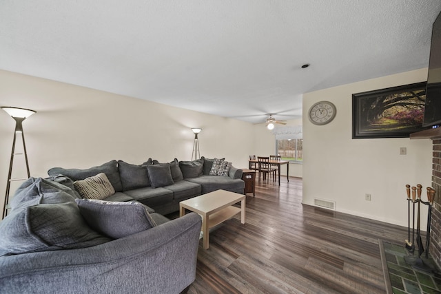 living room featuring a textured ceiling, ceiling fan, dark wood-type flooring, and a brick fireplace