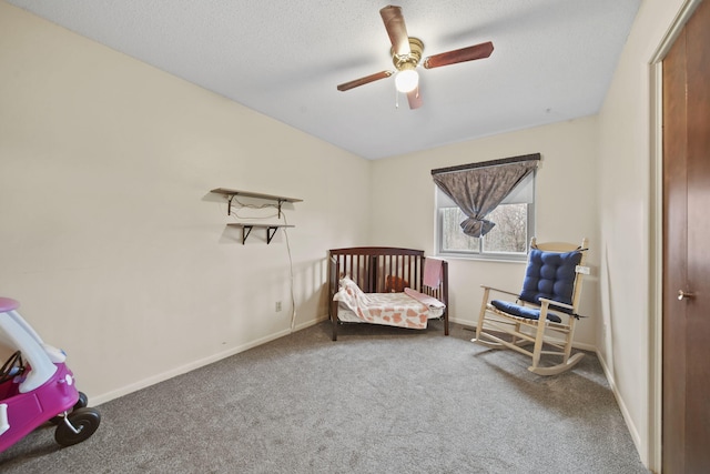 carpeted bedroom with a textured ceiling, a nursery area, and ceiling fan