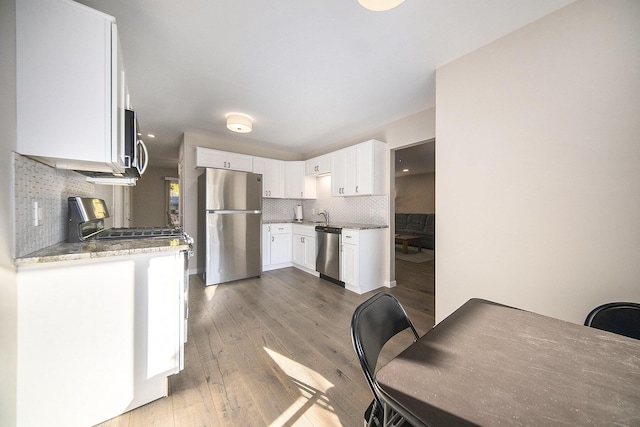 kitchen with light stone countertops, stainless steel appliances, dark hardwood / wood-style flooring, decorative backsplash, and white cabinets