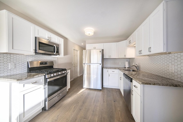 kitchen featuring white cabinets, appliances with stainless steel finishes, light hardwood / wood-style floors, and dark stone counters