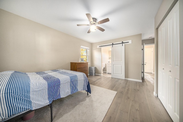 bedroom with ceiling fan, a barn door, light hardwood / wood-style flooring, ensuite bathroom, and a closet