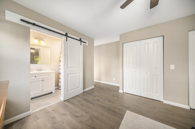 unfurnished bedroom featuring ceiling fan, a barn door, connected bathroom, light hardwood / wood-style floors, and a closet