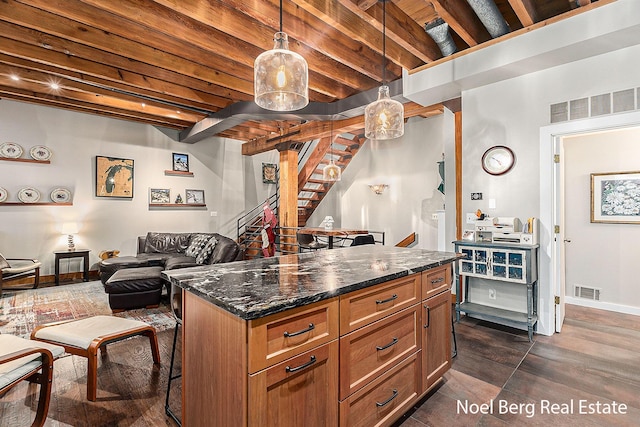 kitchen featuring a kitchen bar, pendant lighting, dark stone countertops, and beam ceiling