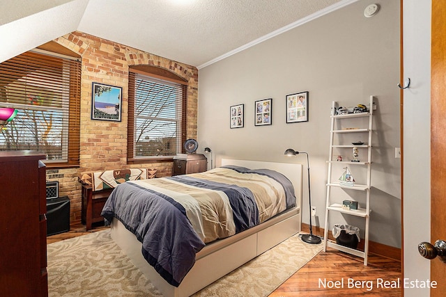 bedroom featuring light hardwood / wood-style floors, lofted ceiling, crown molding, and brick wall