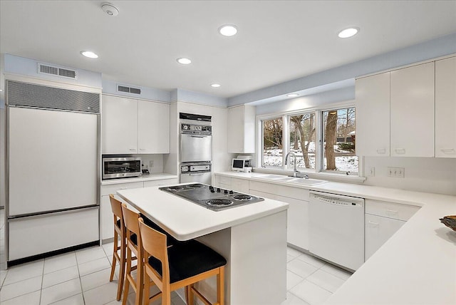 kitchen with black electric stovetop, a kitchen breakfast bar, white dishwasher, sink, and paneled built in refrigerator