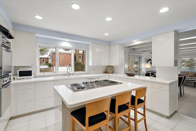 kitchen featuring sink, a kitchen island, kitchen peninsula, a breakfast bar, and white cabinets