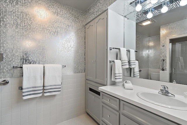 bathroom featuring tile patterned flooring, an enclosed shower, toilet, vanity, and tile walls