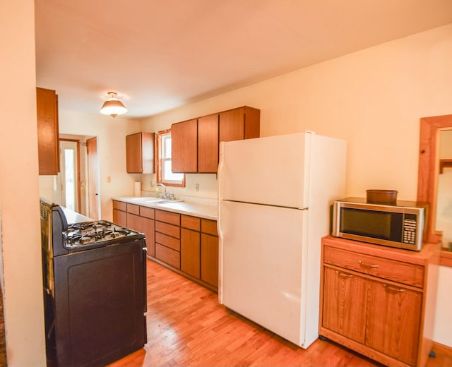 kitchen with gas stove, white fridge, light hardwood / wood-style flooring, and sink