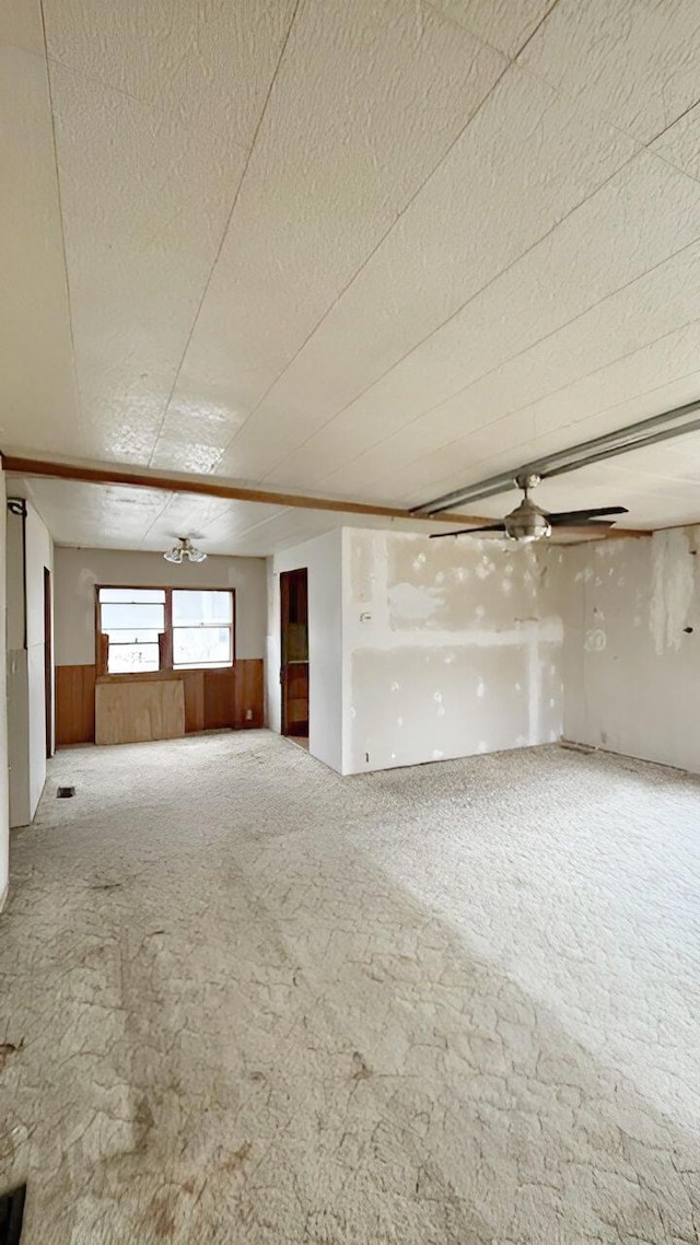 carpeted spare room with a textured ceiling, ceiling fan, and wooden walls