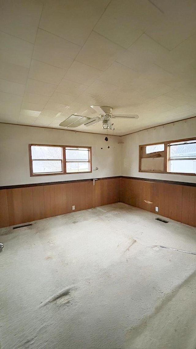 unfurnished room featuring a wealth of natural light, wooden walls, and ceiling fan