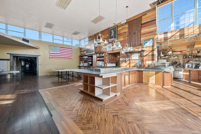 kitchen with wood walls, light brown cabinets, a towering ceiling, and decorative light fixtures