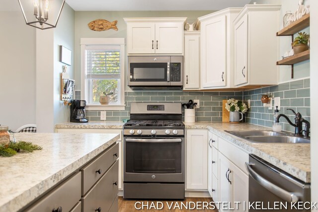 kitchen featuring white cabinets, sink, hanging light fixtures, decorative backsplash, and stainless steel appliances