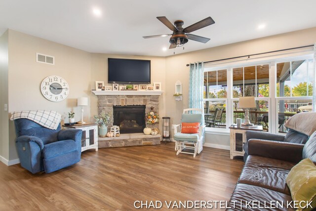 living room with hardwood / wood-style flooring, a stone fireplace, and ceiling fan