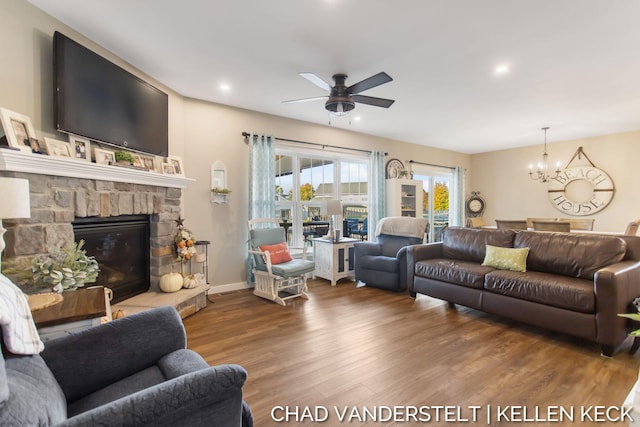 living room with a stone fireplace, hardwood / wood-style floors, and ceiling fan with notable chandelier