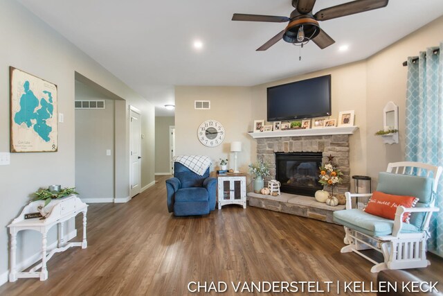 living room with a stone fireplace, ceiling fan, and dark wood-type flooring