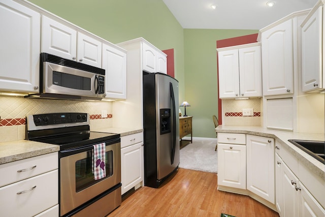 kitchen featuring appliances with stainless steel finishes, light wood-type flooring, backsplash, white cabinets, and lofted ceiling