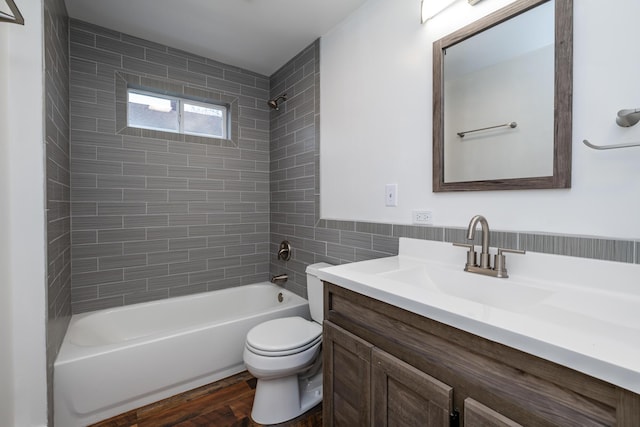 full bathroom with hardwood / wood-style floors, vanity, tiled shower / bath, toilet, and tile walls