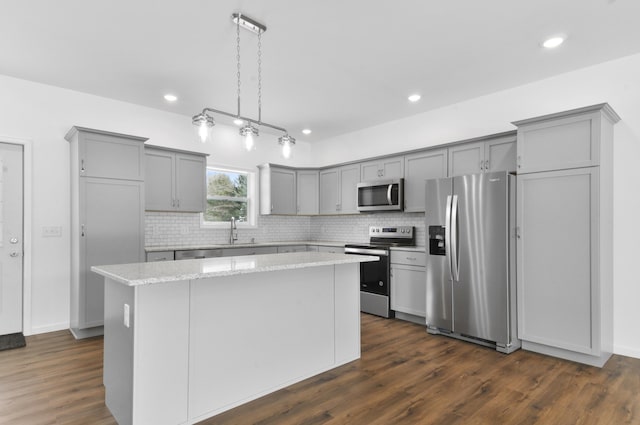 kitchen with pendant lighting, dark hardwood / wood-style floors, light stone countertops, appliances with stainless steel finishes, and a kitchen island