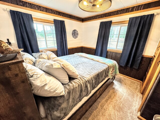 bedroom with carpet flooring, multiple windows, wood walls, and crown molding