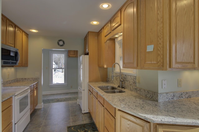 kitchen featuring light stone counters, white appliances, sink, light brown cabinets, and dark tile patterned flooring