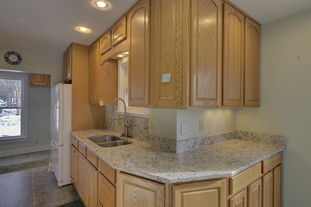 kitchen with white fridge, light stone counters, sink, and light brown cabinetry